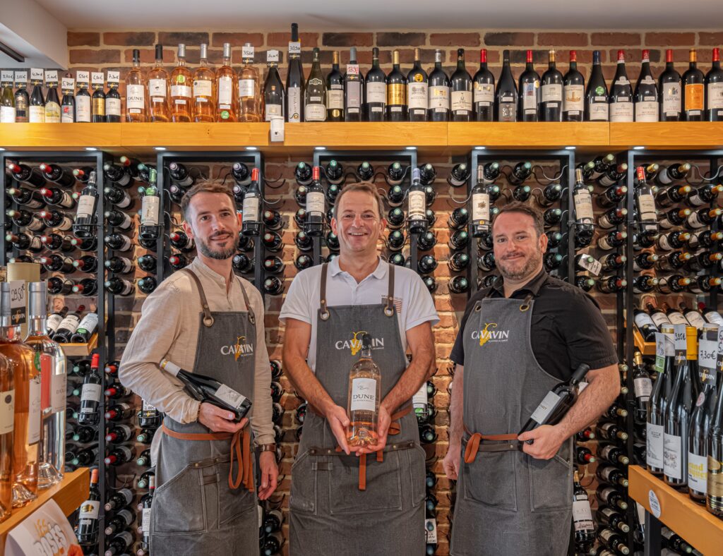 Trois cavistes CAVAVIN dans leur cave, entourés de bouteilles de vin